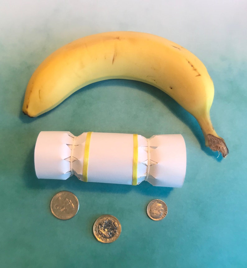 May include: A white paper Christmas cracker with yellow ribbon, a yellow banana, and three gold coins on a teal background.