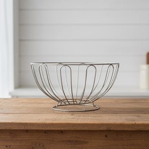 Peut inclure: Un saladier en fil d'argent de forme arrondie avec une base circulaire. Le bol est composé de boucles de fil verticales reliées en haut et en bas. Il repose sur une table en bois.