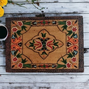 May include: A decorative wooden tray with a hand-painted design featuring colourful flowers and geometric patterns. The tray has a brown wooden frame and a light brown background.