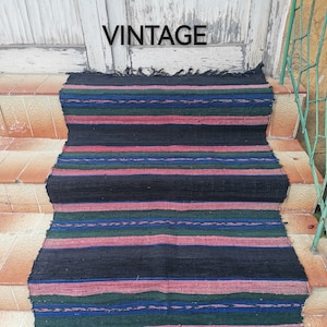 Puede incluir: Una alfombra vintage a rayas en tonos negro, rosa, verde y azul. La alfombra está colocada en un tramo de escaleras.