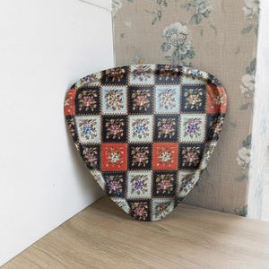 May include: A decorative serving tray with a unique shape and a floral pattern. The tray features a checkered design with squares of red, black, and blue, each containing a floral motif. The tray is resting on a wooden surface.