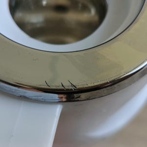 May include: Close-up of a white and silver tea kettle. The silver rim shows minor scratches. The white handle is visible on the bottom left.