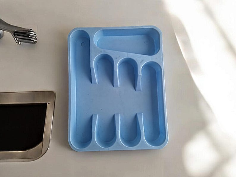 K&ouml;nnte beinhalten: Ein hellblaues Plastik-Bestecktablett mit sechs F&auml;chern f&uuml;r Besteck. Das Tablett ist rechteckig und daf&uuml;r ausgelegt, Gabeln, L&ouml;ffel und Messer aufzunehmen.