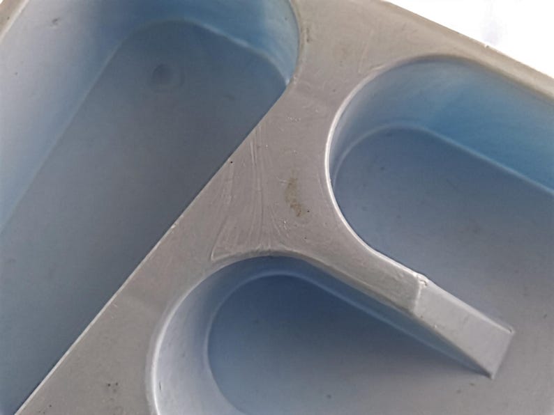 K&ouml;nnte beinhalten: Nahaufnahme einer grauen Plastikform mit drei ovalen Vertiefungen. Die Form ist zum Herstellen von Eisw&uuml;rfeln oder anderen kleinen Gegenst&auml;nden gedacht.