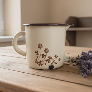 Op de afbeelding: Een witte keramische mok met een zwart handvat en de tekst "But First, Coffee" in een zwarte, handgeschreven lettertype. De mok staat op een wit oppervlak.