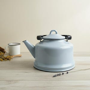 May include: A pale blue enamel kettle with a black handle and lid. A white mug, a wooden spoon, and a small hessian bag filled with dried herbs are next to the kettle. A sprig of lavender is in the foreground.