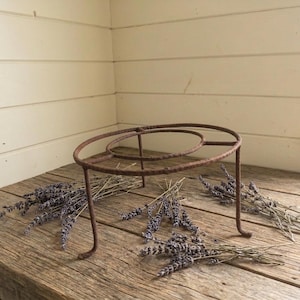 Puede incluir: Un soporte de metal marrón oxidado con diseño circular, sobre una superficie de madera envejecida. Ramos de lavanda seca se disponen alrededor, creando una estética rústica.