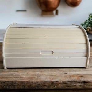 Puede incluir: Una caja de pan blanca con tapa enrollable. La caja tiene una pequeña manija en la parte delantera.