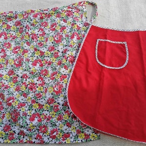 Peut inclure: Un tablier rouge avec une bordure blanche et une poche blanche. Le tablier a un imprimé floral au dos.