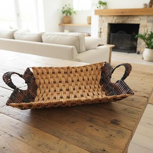 Peut inclure: Un plateau rectangulaire en osier tressé avec deux poignées incurvées. Le plateau présente une palette de couleurs naturelles, beige et marron, et est posé sur une table en bois rustique. Le plateau est conçu pour servir ou décorer.