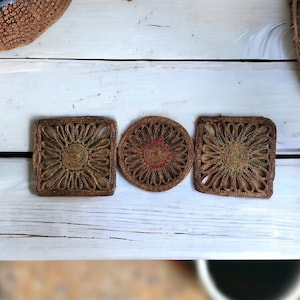 Könnte beinhalten: Drei gewebte Untersetzer in quadratischer, runder und quadratischer Form. Die Untersetzer sind aus natürlichen Materialien gefertigt und haben ein braunes und grünes Farbschema.