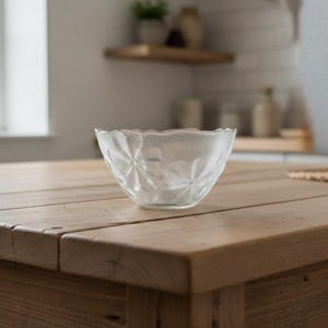 Könnte beinhalten: Eine klare Glasschale mit floralem Muster steht auf einem Holztisch. Die Schale hat einen gewellten Rand und eine strukturierte Oberfläche. Der Tisch ist aus hellem Holz.