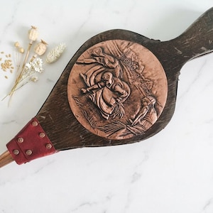 Può includere: Antico mantice in legno con un medaglione in rame raffigurante una scena in rilievo. Il mantice ha una finitura in legno scuro, un accento in pelle rossa e rivetti in rame. Un pezzo decorativo per un camino o un arredamento rustico.