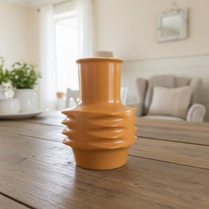 Op de afbeelding: Een oranje keramische vaas met een getextureerd, geribbeld ontwerp. De vaas is cilindrisch met een uitlopende bovenkant en staat op een houten tafel. De vaas is ongeveer 25 cm hoog.