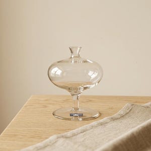 Peut inclure: Une tasse en céramique blanche avec une anse noire et le texte "But First, Coffee" dans un style manuscrit. La tasse est posée sur une surface blanche. La tasse mesure environ 10 cm de haut.