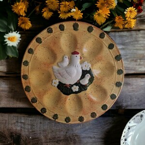 May include: A yellow ceramic egg plate with a green and brown border. The plate features a white ceramic hen and chicks design.