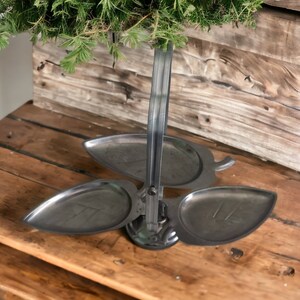 May include: A three-tiered serving tray made of metal, shaped like leaves, with a handle. The tray is silver in color and has a rustic wooden background.