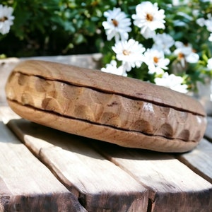 Può includere: Una ciotola di legno con un bordo scolpito e testurizzato. La ciotola è di colore marrone chiaro e ha una finitura in legno naturale. È appoggiata su una superficie di legno.