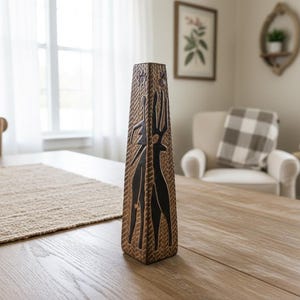 Könnte beinhalten: Eine hohe, rechteckige braune Vase mit strukturierter Oberfläche und schwarzen abstrakten Designs. Die Vase steht auf einem hellen Holztisch, mit einem gewebten Tischset. Die Vase ist etwa 30 cm hoch.