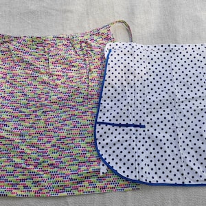 Könnte beinhalten: Zwei Stoffschürzen mit unterschiedlichen Mustern. Eine Schürze ist weiß mit blauen Punkten und einem blauen Saum. Die andere Schürze ist weiß mit einem mehrfarbigen Punktmuster.