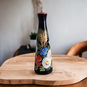 May include: A dark blue ceramic vase with a floral design. The vase is decorated with red, white, yellow, and blue flowers and leaves. The vase is sitting on a wooden surface.