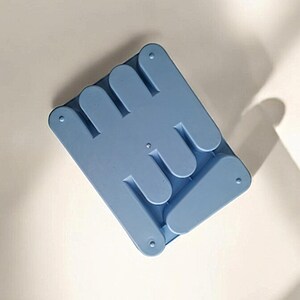 K&ouml;nnte beinhalten: Ein hellblauer Telefonst&auml;nder aus Kunststoff mit einem einzigartigen Design, der sich zum einfachen Verstauen zusammenklappen l&auml;sst.