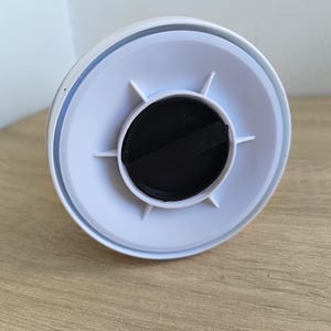 May include: A white plastic object with a circular design, featuring a black center and radiating white supports. The object is set against a light wooden surface.