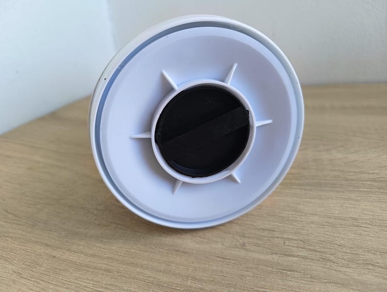 May include: A white plastic object with a circular design, featuring a black center and radiating white supports. The object is set against a light wooden surface.