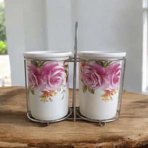 May include: A set of two white ceramic utensil holders with a pink rose floral design, in a silver metal stand.