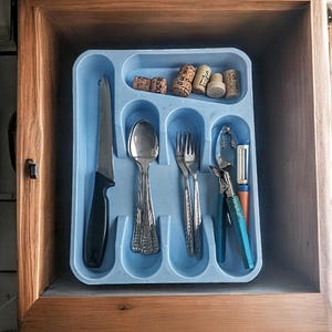 K&ouml;nnte beinhalten: Ein blaues Besteckfach mit einem Messer, einem L&ouml;ffel, einer Gabel, einem Nussknacker und einem Gem&uuml;sesch&auml;ler. Es befinden sich auch f&uuml;nf Weinkorken im Fach.