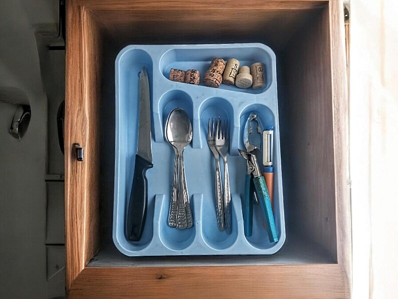 K&ouml;nnte beinhalten: Ein blaues Besteckfach mit einem Messer, einem L&ouml;ffel, einer Gabel, einem Nussknacker und einem Gem&uuml;sesch&auml;ler. Es befinden sich auch f&uuml;nf Weinkorken im Fach.