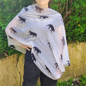 May include: A light-colored scarf featuring a repeating pattern of black horse silhouettes. The scarf has the text "YO MR WHITE" printed on it. The scarf is draped over a person.
