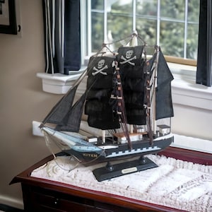 May include: A black and white model pirate ship with black sails and skull and crossbones flags. The ship is sitting on a white sand base and is labeled "Kiten" and "Blackadder".