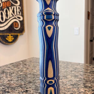 K&ouml;nnte beinhalten: Ein hoher Pfefferm&uuml;hle aus Holz mit blau-wei&szlig;em Streifenmuster. Das Design zeigt abwechselnde B&auml;nder aus Blau und Naturholzt&ouml;nen. Die M&uuml;hle hat einen bauchigen Kopf und einen zylindrischen K&ouml;rper. H&ouml;he ca. 20 cm.