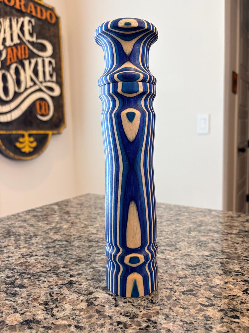 K&ouml;nnte beinhalten: Ein hoher Pfefferm&uuml;hle aus Holz mit blau-wei&szlig;em Streifenmuster. Das Design zeigt abwechselnde B&auml;nder aus Blau und Naturholzt&ouml;nen. Die M&uuml;hle hat einen bauchigen Kopf und einen zylindrischen K&ouml;rper. H&ouml;he ca. 20 cm.