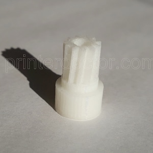 May include: White plastic gear with a round base and a toothed top. The gear is about 2 inches tall.