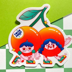 Puede incluir: Dos cerezas de dibujos animados con caras y piernas, que llevan zapatillas deportivas. Las cerezas son rojas y naranjas con un tallo y hojas verdes. El texto "Twin Fruit" est&aacute; en una de las cerezas.