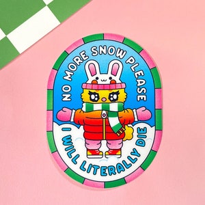 Puede incluir: Una pegatina redonda con un borde verde, rosa y azul. La pegatina presenta un conejito de dibujos animados que lleva una chaqueta roja, una bufanda verde y un gorro rosa. El texto de la pegatina dice "No More Snow Please I Will Literally Die."