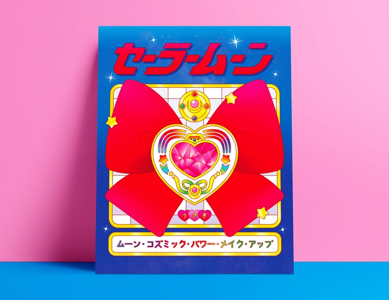 May include: A blue and white poster with the Japanese text "セーラームーン" and a red bow with a gold heart-shaped brooch in the center. The text at the bottom of the poster reads "ムーン・コズミック・パワー・メイク・アップ".
