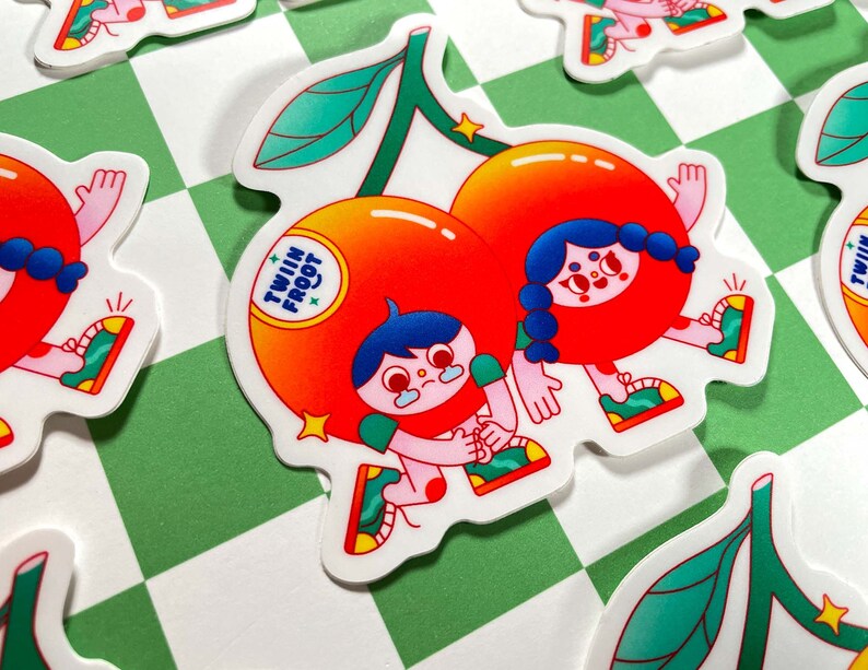 Puede incluir: Dos personajes de dibujos animados vestidos de cerezas con hojas verdes, tomados de la mano. Las cerezas son rojas y naranjas con contornos blancos. Los personajes tienen el pelo azul y sonr&iacute;en. El texto "Twin Fruit" est&aacute; escrito en la cereza de la izquierda.