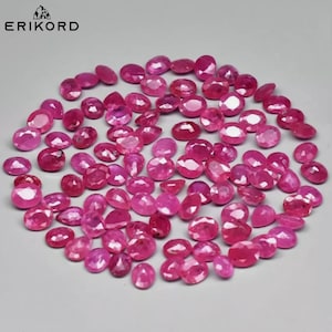 May include: A collection of approximately 50 oval-shaped pink gemstones. The gemstones are arranged in a loose pile on a white surface.