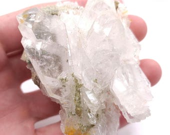 May include: A cluster of clear quartz crystals with a green and yellow mineral inclusion. The crystals are arranged in a fan shape and have a translucent appearance.