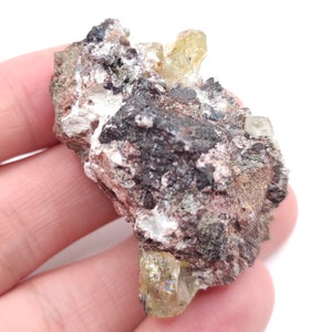 Puede incluir: Una roca áspera de color gris, marrón y verde con varios cristales amarillos que sobresalen de ella.