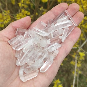 May include: A collection of clear quartz crystal points, also known as rock crystals, in various sizes and shapes. The crystals are smooth and translucent, with a slight sparkle.