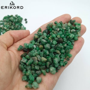 May include: A close-up of a handful of small, green emerald gemstones. The stones are rough and have a natural, unpolished look.