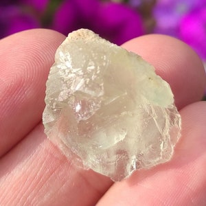 Könnte beinhalten: Ein kleiner, durchscheinender grüner Fluoritkristall mit einer rauen, unregelmäßigen Form. Der Kristall hat eine hellgrüne Farbe und ist leicht trüb.