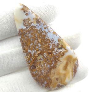 May include: A teardrop-shaped, white, brown, and gold agate pendant with a mottled, marbled pattern.