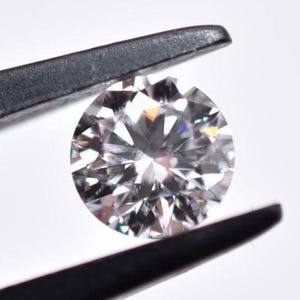 Peut inclure: Un diamant rond brillant, transparent, tenu par des pinces. Le diamant a un haut degré d'éclat et de brillance.