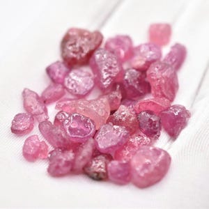 Könnte beinhalten: Ein Haufen roher rosa Rubin-Edelsteine. Die rohen Edelsteine sind in verschiedenen Größen und Formen.