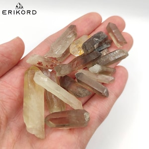 Puede incluir: Una colección de puntas de cristal de cuarzo ahumado en varios tonos de marrón, amarillo y transparente. Los cristales son en bruto y tienen una textura natural y rugosa.